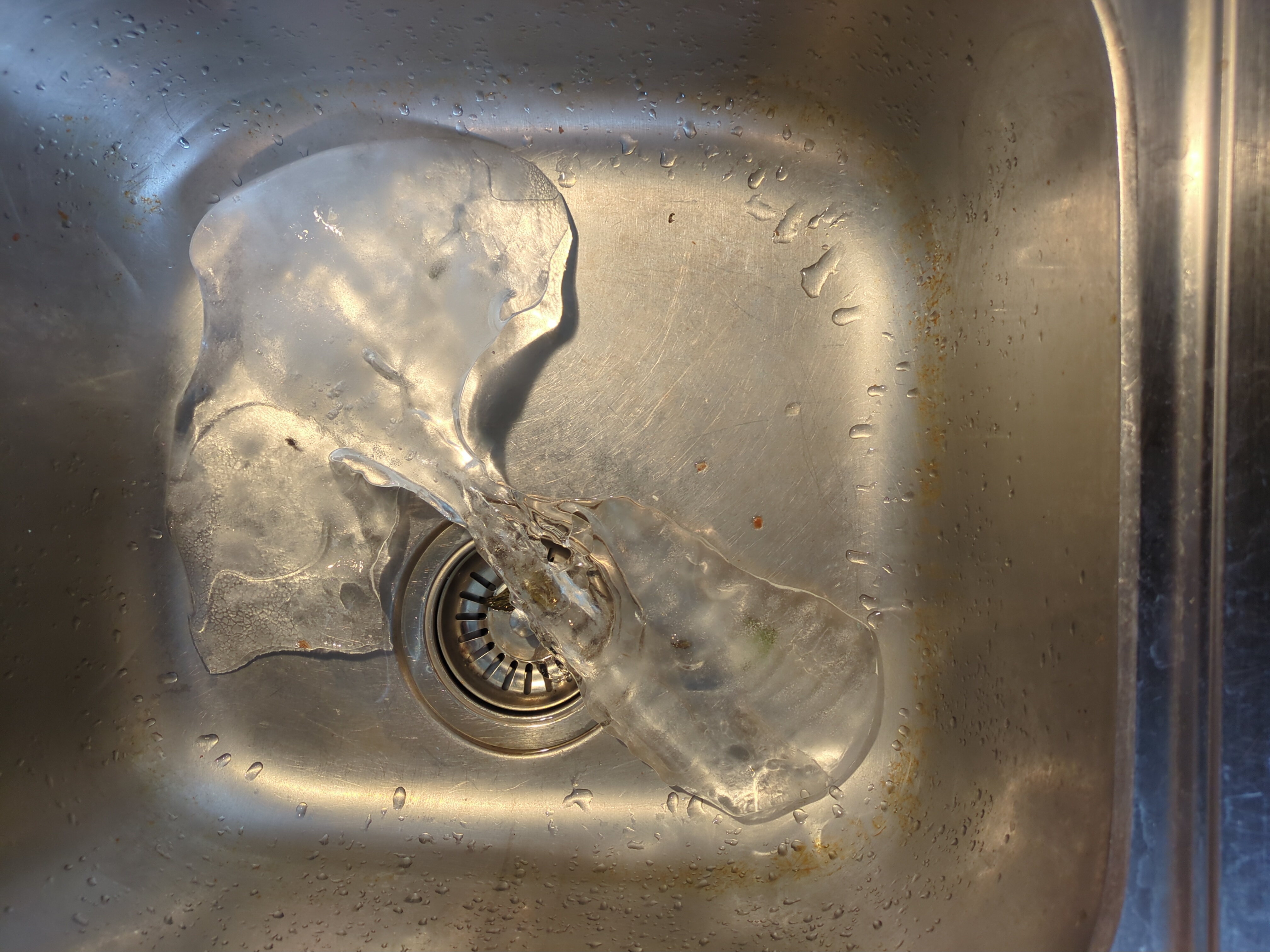 An irregular chunk of ice at the bottom of a metal sink.