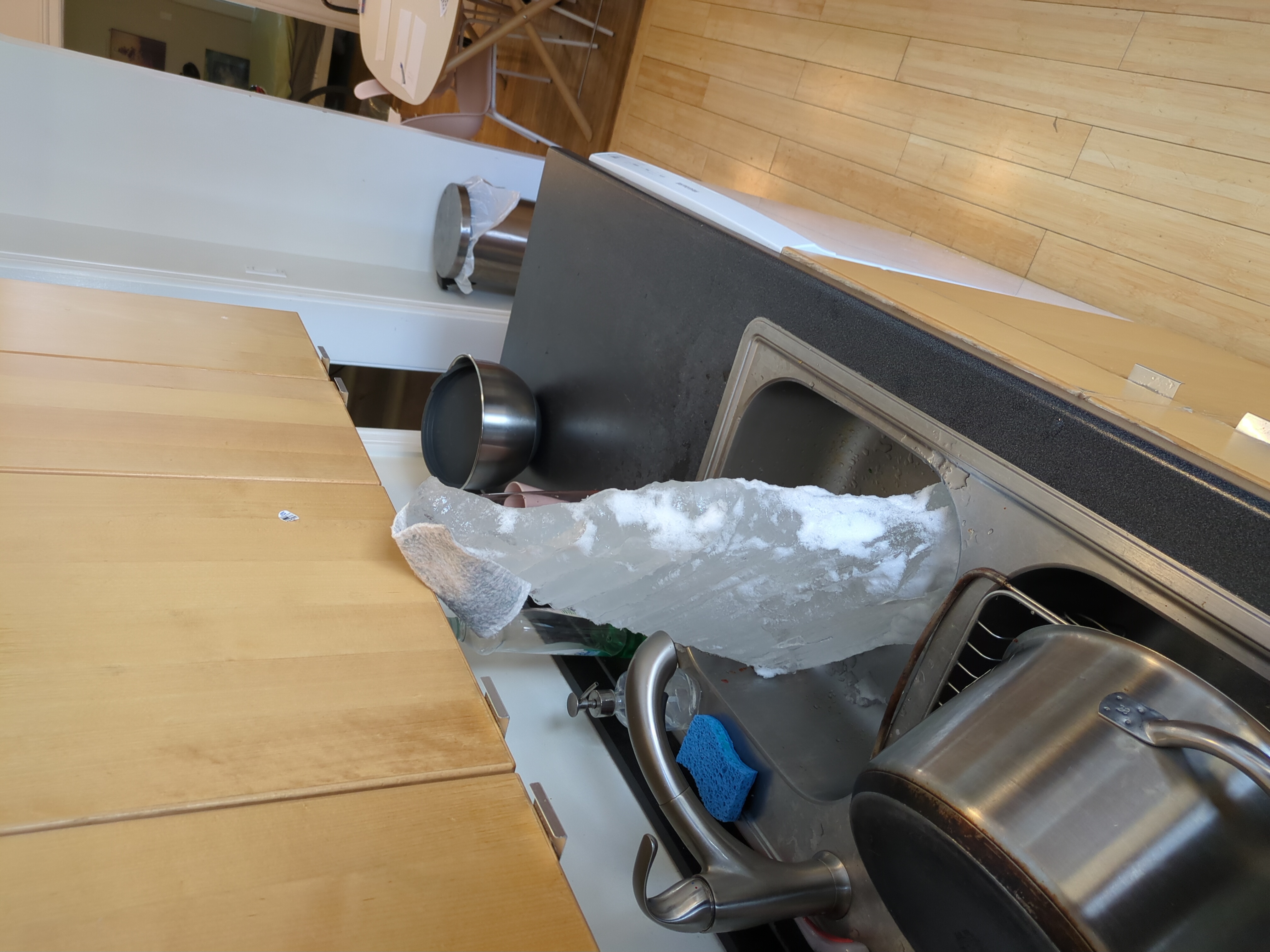 A large, irregular block of ice in a kitchen sink. It is the top of a group of icicles.